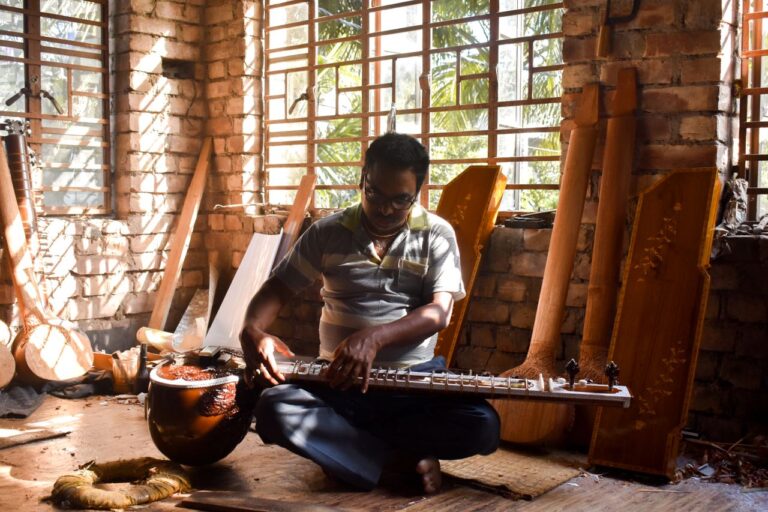 Artisan in Kolkata, India, crafting a traditional musical instrument in a sunlit room.